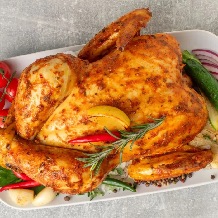 Egész sült csirke aranybarnára sütve fehér tepsiben, salátaágyon, friss rozmaring ággal tálalva