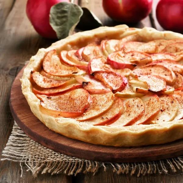 Almás sütemény torta vékony almadarabokkal a tetején, fahéjas fűszerrel megszórva egy tálon.