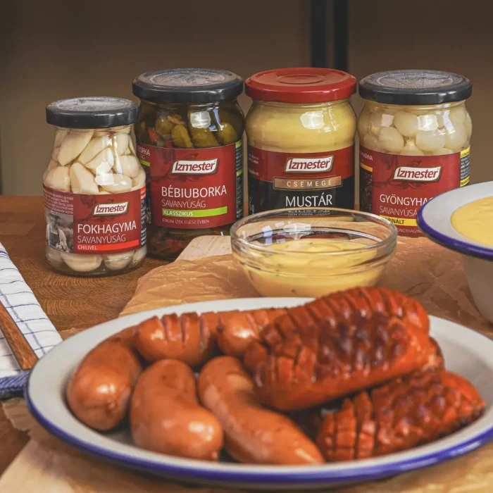 Cheddar szósz sült kolbásszal tányéron, mögötte üveges mustár.