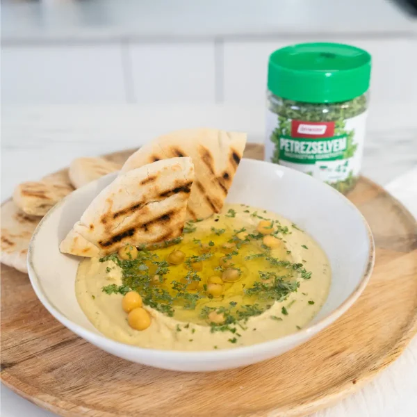 Hummusz tálban, pitával és petrezselyemel tálalva, mellette üveges fagyasztva szárított petrezselyem termék