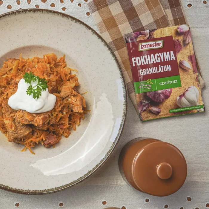 Székelykáposzta fehér tányérban asztalon, mellette kockás konyharuha és egy tasak fokhagyma granulátum