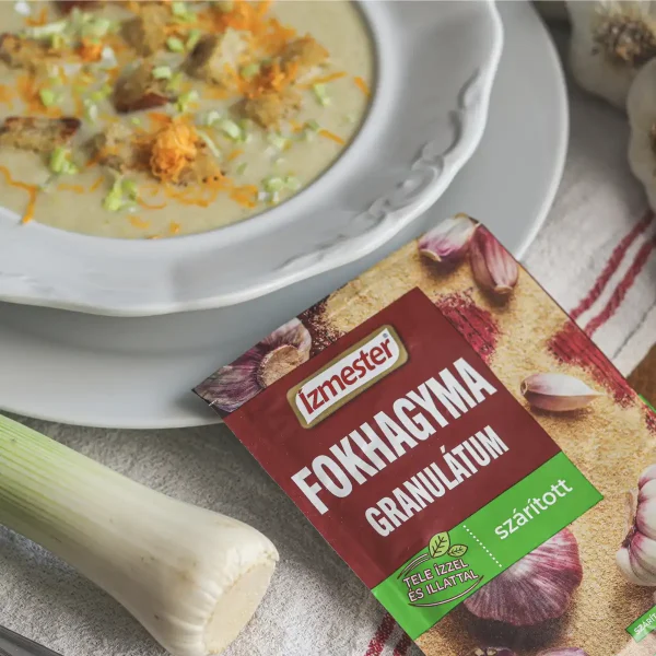 Póréhagyma krémleves fehér tányéron mellette egy tasak fokhagyma granulátum