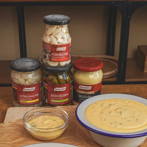 Ízmester savanyúságok (fokhagyma, gyöngyhagyma, bébiuborka) és mézes mustár üvegek, cheddar szósszal tálalva.
