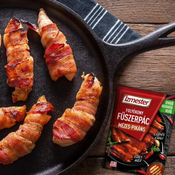 Baconba göngyölt csirkemell csíkok serpenyőben mellette egy tasak mézes-pikáns folyékony fűszerpác