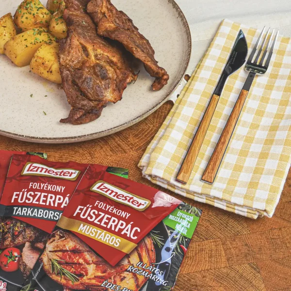 Sült hús és sült kockázott burgonya fehér tányéron, mellette evőeszközökkel és 2 tasak folyékony fűszerpáccal