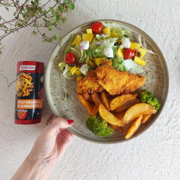 Egy tányérban bundás rántott csirke steak burgonyával, friss salátával, mozzarella golyókkal, paradicsommal, salátalevéllel, brokkolival tálalva, mellette sült krumpli fűszer termék