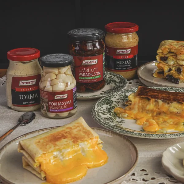 Négysajtos szendvics tányéron tálalva, mögötte Ízmester reszelt torma, fokhagyma és bébiuborka savanyúság, mustár üvegben