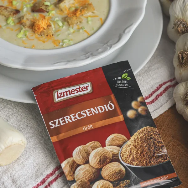 Póréhagyma krémleves fehér tányérban mellette egy tasak őrölt szerecsendió