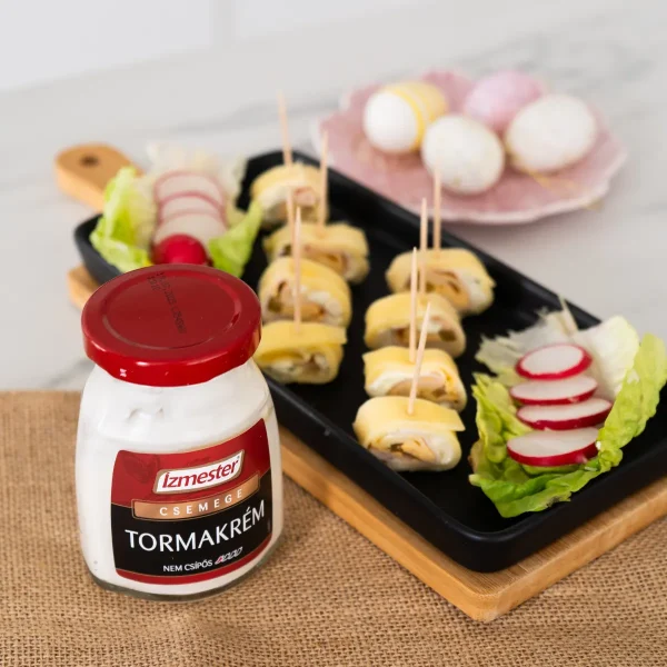 Vendégváró hideg húsvéti sonkatekercs falatok fogpiszkálóval átszúrva, retekkel, üveges tormakrémmel egy asztalon