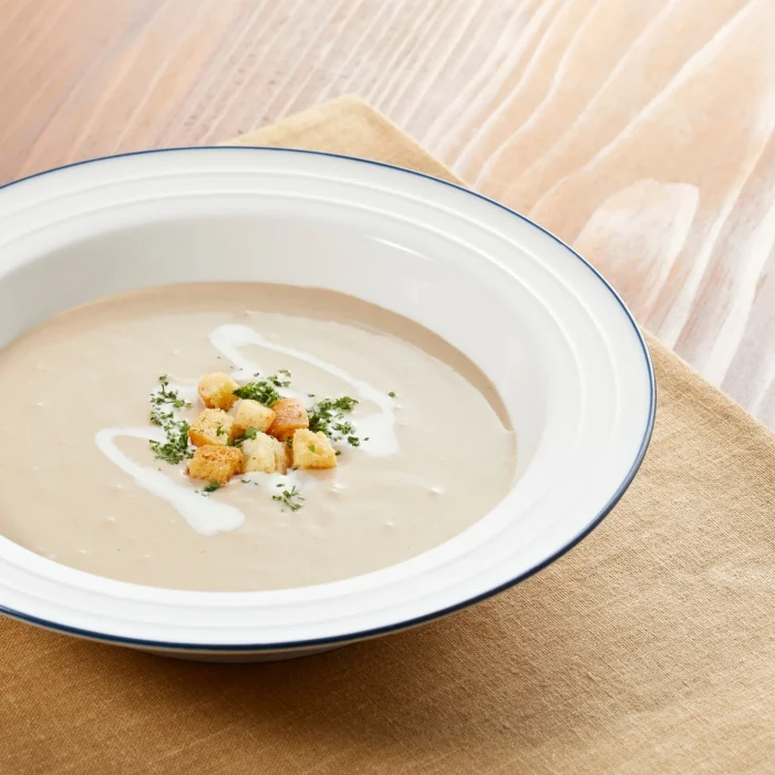 Gombakrémleves fehér tányérban, pirított kenyérkockákkal, krutonnal és zöldfűszerrel tálalva