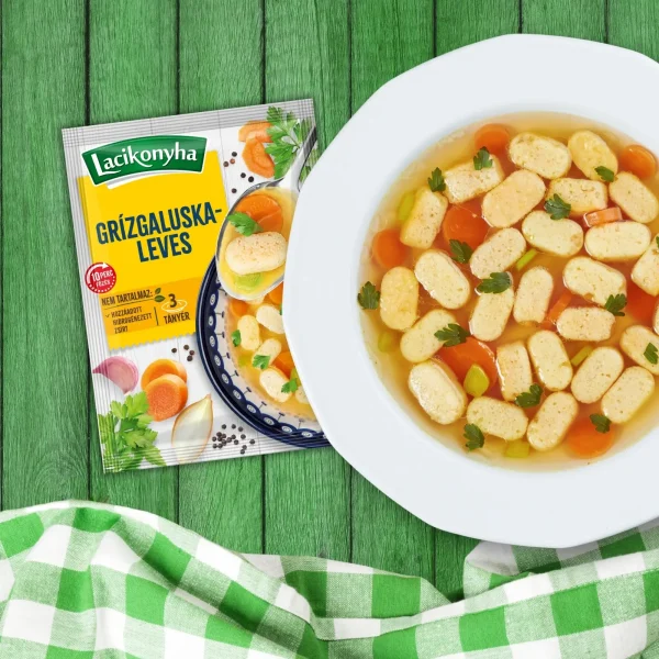 Grízgaluskaleves házias stílusú levespor tasak faerezetes asztalon, mellette fehér tányérban grízgaluskaleves és zöld-fehér kockás terítővel