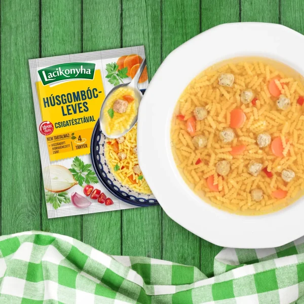 Húsgombócleves házias stílusú levespor tasak faerezetes asztalon, mellette fehér tányérban húsgombócleves és zöld-fehér kockás terítővel