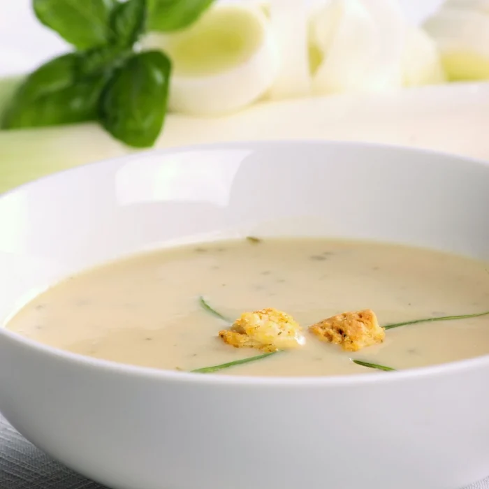 Póréhagyma krémleves fehér tálban, pirított kenyérkockákkal, krutonnal tálalva