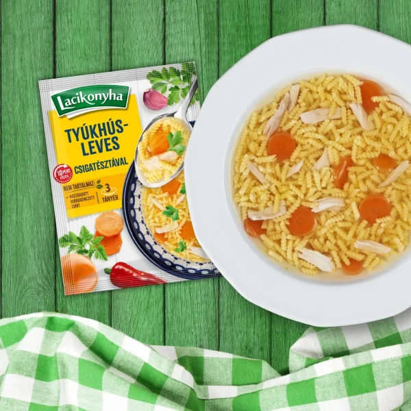 Tyúkhúsleves csigatésztával házias stílusú levespor tasak faerezetes asztalon, mellette fehér tányérban tyúkhúsleves és zöld-fehér kockás terítővel