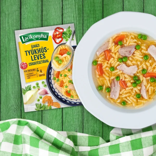 Újházi tyúkhúsleves csigatésztával házias stílusú levespor tasak faerezetes asztalon, mellette fehér tányérban tyúkhúsleves és zöld-fehér kockás terítővel