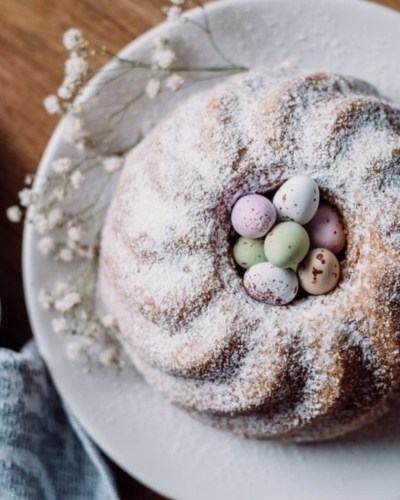 Húsvéti kuglóf bazsalikommal és joghurttal, porcukorral megszórva tányéron, húsvéti dísztojásokkal tálalva
