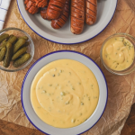 Házi cheddar szósz sült kolbásszal, uborka savanyúsággal tálalva