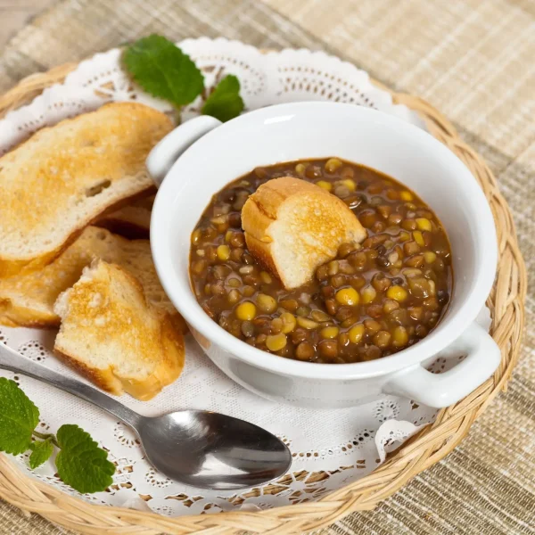 egy fehér tálban pirított olajos kenyérrel tálalva lencsefőzelék