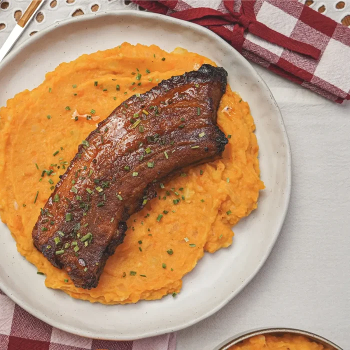 Narancsos sült oldalas metélőhagymával megszórva, édesburgonyapürével tálalva, felülnézetből, fehér tányéron