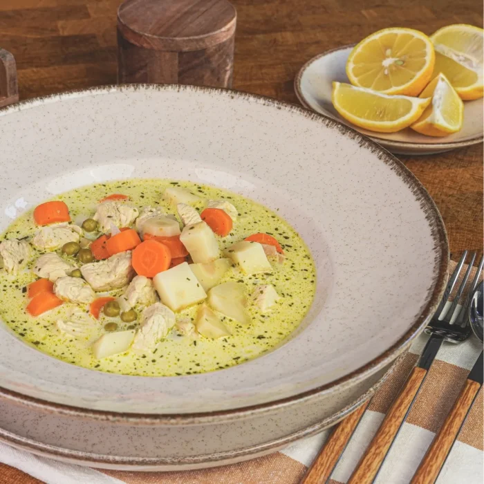 Egytál tárkonyos raguleves csirkével fa asztalon mély tányérban, mellette dekorációként evőeszköz, félbevágott citrom