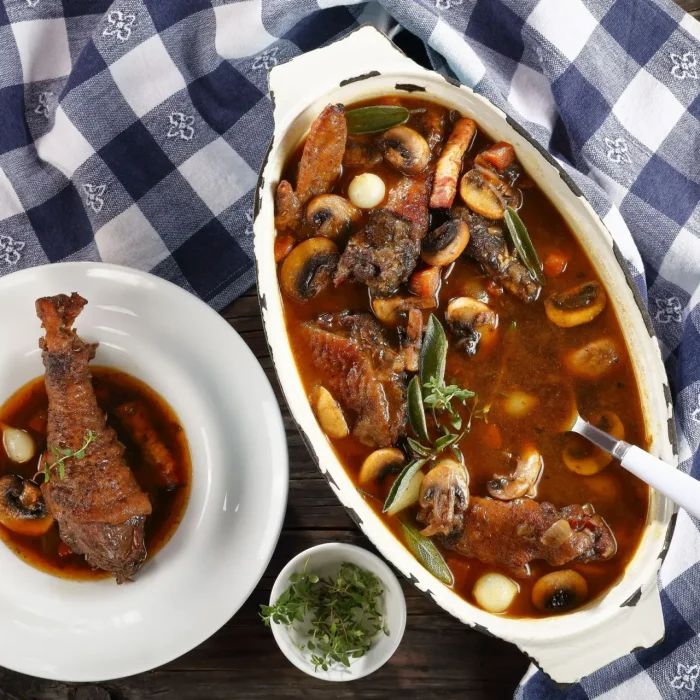 Sült szárnyas comb gombás mártással tálalva, gyöngyhagymával sütve fehér sütőtálban, kék terítős asztalon