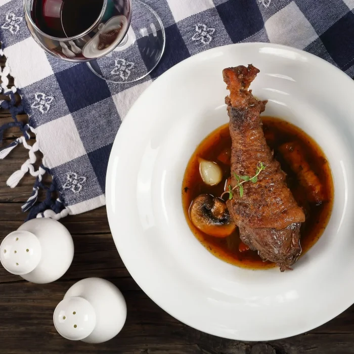 Sült szárnyas comb gombás mártással tálalva, gyöngyhagymával sütve fehér mélytányérban, kék terítős asztalon