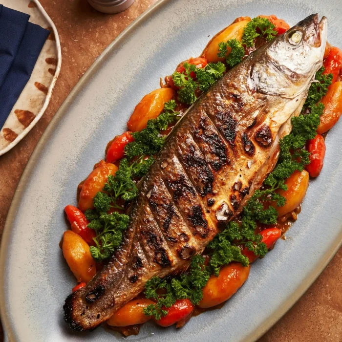 Egészben sült hal zöldségágyon fehér tányéron