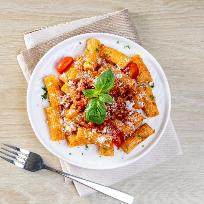 Paradicsomos tészta sajttal és bazsalikommal fehér tányérban felülnézetből