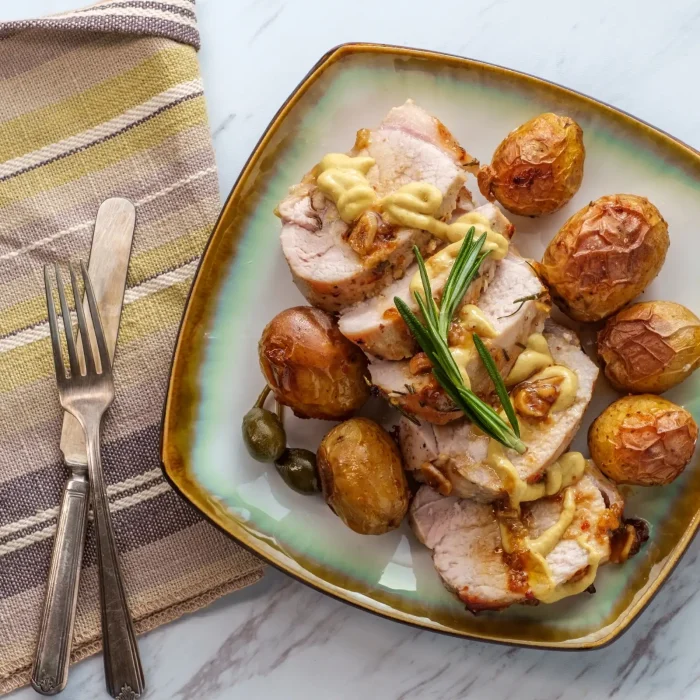 Sült hús burgonyával tányéron, mellette evőeszközök