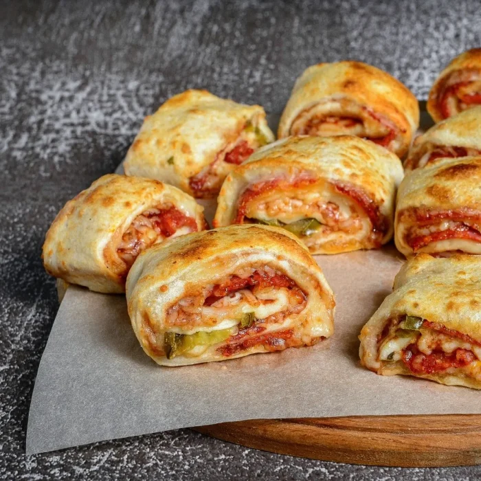 Szárított paradicsommal töltött pizza tekercsek sajttal egy fa deszkán tálalva