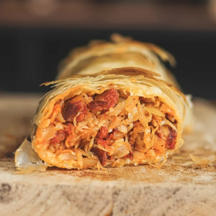 Káposztás, kolbászos rétes félbevágva fa vágódeszkán tálalva