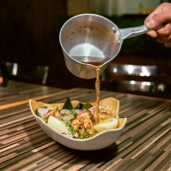 erőlevessel öntenek le egy tál zöldséget, húst és főtt tojást