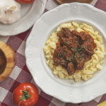 Marhapörkölt tésztával tányéron, mellette paradicsommal