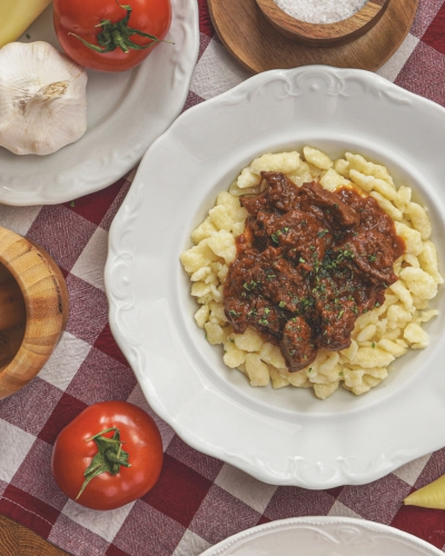 Marhapörkölt tésztával tányéron, mellette paradicsommal
