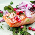 Sült lazac gránátalmával és zöldspárgával tányéron tálalva lilahagymával a tetején