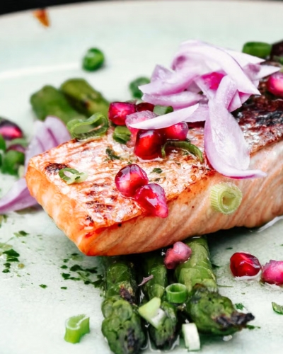 Sült lazac gránátalmával és zöldspárgával tányéron tálalva lilahagymával a tetején