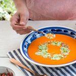 Sült paprika krémleves nyári asztalon tálalva, egy ember tejfölt kanalaz a levesre