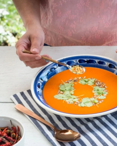 Sült paprika krémleves nyári asztalon tálalva, egy ember tejfölt kanalaz a levesre