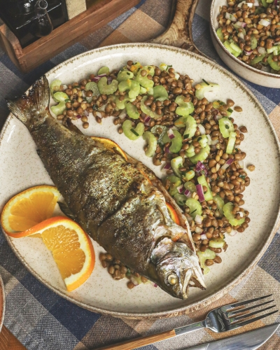 Egészben sült pisztráng zelleres lencsesalátával, félbevágott narancsszelettel tálalva tányéron