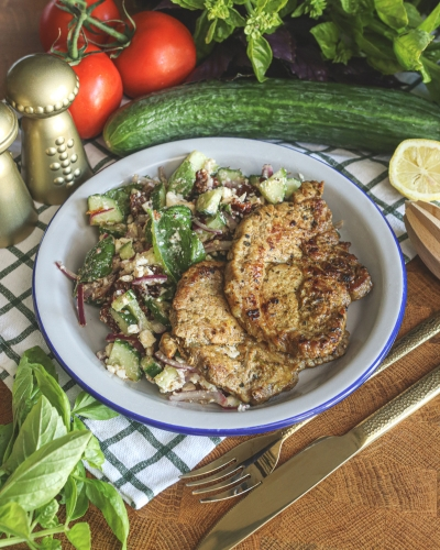 Zöldfűszeres tarja salátával tányérban, mellette uborka, paradicsom, saláta