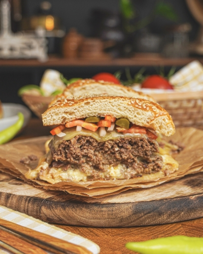 Házi sajtburger félbevágva fa deszkán, uborkával, répával, húspogácsával, sajttal