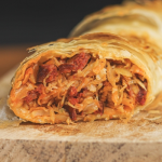 Káposztás-kolbászos rétes félbevágva fa vágódeszkán