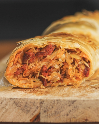 Káposztás-kolbászos rétes félbevágva fa vágódeszkán