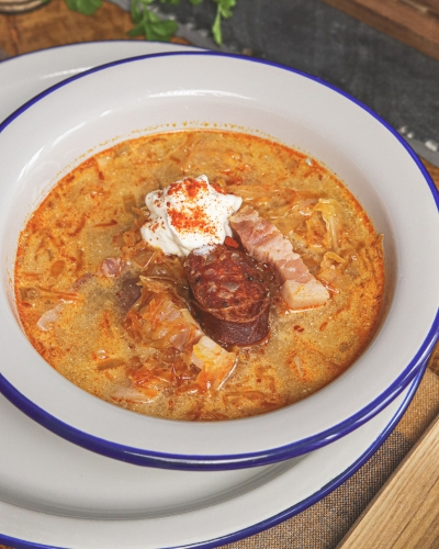 Korhelyleves tejföllel és kolbászkarikával tálalva tányéron