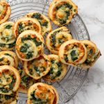 Mini pizzatekercsek sütőrácson tálalva, zöldfűszerrel, sajttal megszórva