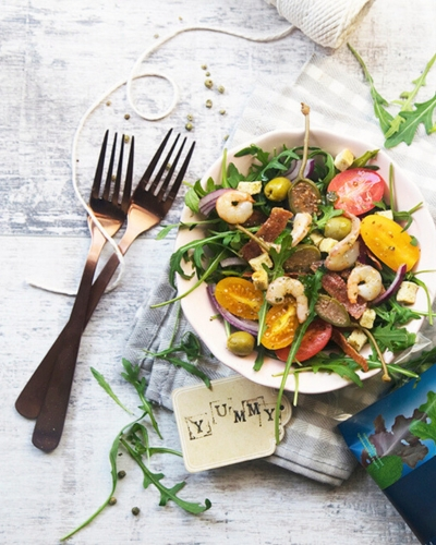 Rukkolasaláta pikáns szalámival evőeszközökkel asztalon tányéron