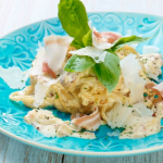 Spagetti carbonara tésztaétel kék tányéron friss zöldfűszerrel és sajttal tálalva
