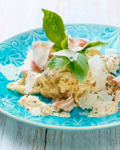 Spagetti carbonara tésztaétel kék tányéron friss zöldfűszerrel és sajttal tálalva