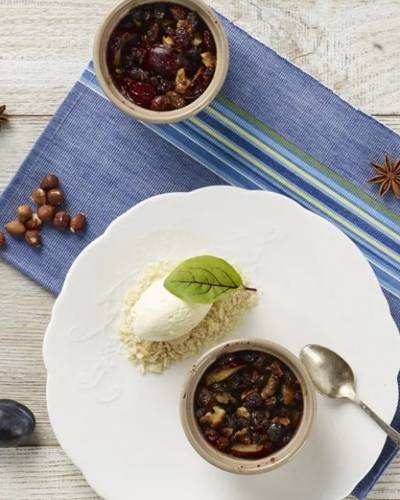 Sült szilva diós morzsában fehér tányéron tálalva friss mentalevéllel