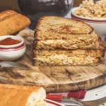 Krémes csirkés grillszendvics félbevágva, fa deszkán tálalva